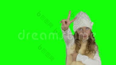 穿白色针织帽子的年轻女孩展示手势。 胜利标志和竖起大拇指的手势.. 年轻女孩的手势。 新年