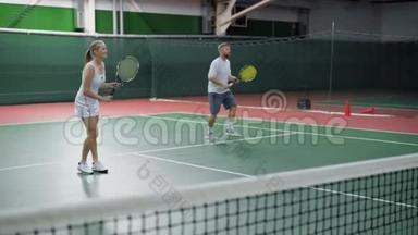 快乐夫妻在室内球场打网球的形象。 穿着运动服装的年轻人在一起