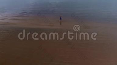 空中：年轻女子穿着蓝色鲜艳的裙子<strong>走来走</strong>去-浅水区的浅黄色日落景观在波罗的海。