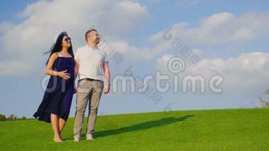 年轻夫妇期待着有个孩子。 丈夫和他怀孕的妻子站在草地上，<strong>展望未来</strong>