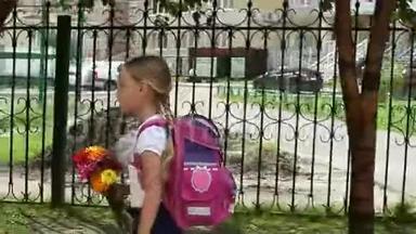 女孩沿着铁栅栏<strong>快速行走</strong>，带着背包和鲜花去学校。 回到学校的概念。 金发少女