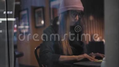 一个<strong>时</strong>髦的<strong>时</strong>髦女人坐在咖啡馆里找一张桌子，<strong>打开</strong>笔记本电脑，开始工作。 从窗口观看