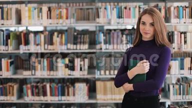 微笑的女学生拿着一本书站在图书馆的书架前