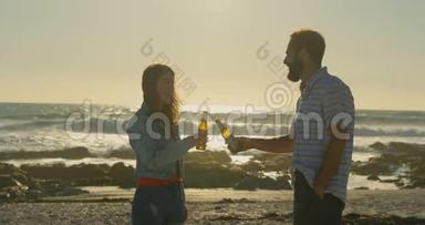 年轻夫妇在阳光明媚的4k日在海滩上<strong>品尝啤酒</strong>瓶