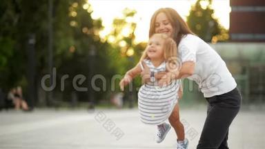 美丽年轻的母亲<strong>托起</strong>女儿在城市广场日落时在户外玩耍。 快乐的小女孩