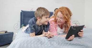 <strong>幸福的</strong>母亲和儿子把平板电脑躺在卧室里，家庭一起度过<strong>时光</strong>