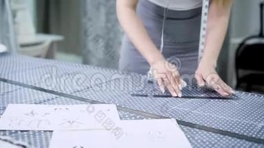 年轻的女设计师站在裁剪工作室的桌子旁，用粉笔和规则在布上做线条