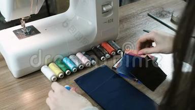 裁缝在桌子上拿起一根线对织物和皮革。 背景中的缝纫机..