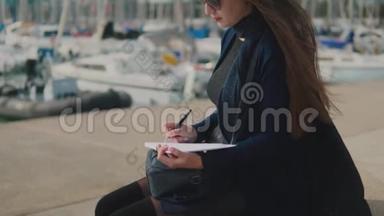 女人在她的户外素描书上画素描。 背景游艇