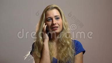 美丽的金发女郎穿着蓝色礼服，讲电话，在工作室获得愉快的邀请