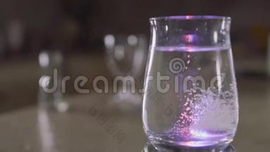 泡腾片落入一个装有水和闪闪发光的彩色灯光的玻璃中