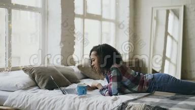 漂亮的混血少女使用笔记本电脑清洗，分享躺在家里床上的社交媒体