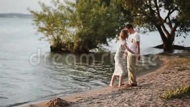 男人和女人晚上在河岸上散步。 美丽的一对情侣在日落时拥抱在水边。