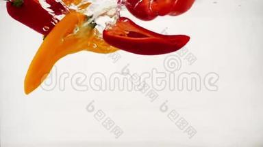 红椒和橙椒随着飞溅和气泡落入水中，慢动作特写镜头