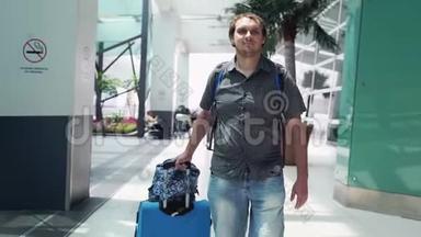 年轻快乐的帅哥，背着背包，在现代机场航站楼里拉着手提箱。 旅行的帅哥走了