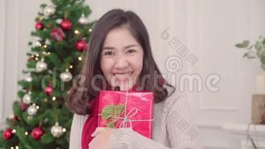 圣诞佳节，快乐的年轻亚洲女人在家的客厅里，捧着圣诞礼物微笑着拍照。