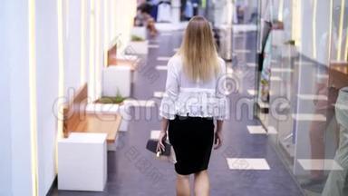 女孩，<strong>高个子</strong>，漂亮的金发女人，沿着商店的窗户，沿着购物中心的大厅走着。