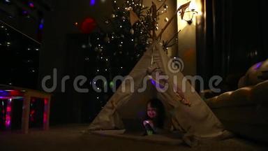 一个小女孩躺在地上，躺在一个圣诞树的背景下，坐在帐篷里讲视频