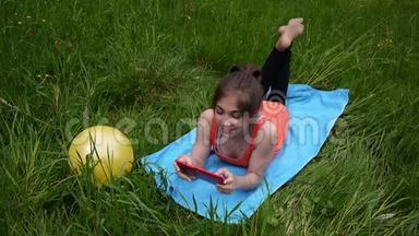 轻松的年轻女孩使用<strong>数字</strong>平板电脑在<strong>乡村</strong>领域。 可爱的少年躺在草地上。 录像片高清拍摄