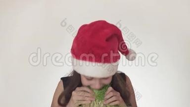 一个漂亮淘气的少女戴着圣诞老人的帽子，<strong>胃口</strong>很大，吃着白色背景的燕麦