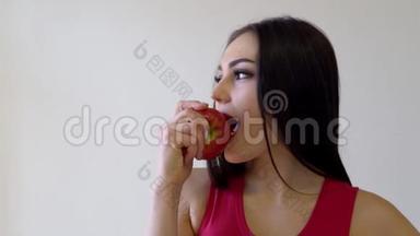 美丽的黑发女孩在白色的苹果上吃红苹果