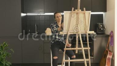 才华横溢的女艺术家在家现代厨房的画布上作画。 女人在家里用丙烯酸涂料画画。