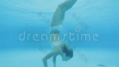 年轻的金发女子在游泳池里表演水下<strong>倒立</strong>