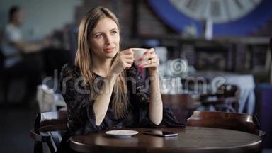 一个金发碧眼的好女人<strong>坐在餐馆</strong>里，望着远处，享受着一杯热咖啡