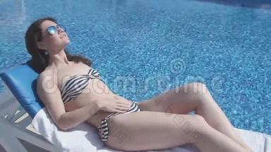 快乐的女人戴着太阳镜在游泳池附近晒太阳，脸上带着微笑