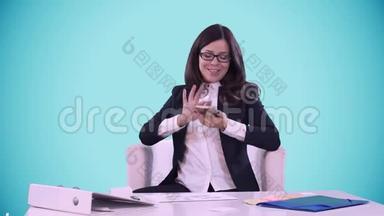 一位身穿商务服、笑容满面的年轻黑发女子在镜头前露出大拇指。 她坐在办公桌后面的办公室里。