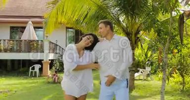 情侣漫步在别墅附近的热带花园里，欢乐的男人和女人在户外亲吻度假的情侣