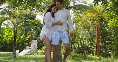 情侣漫步在别墅附近的热带花园里，欢乐的男人和女人在户外亲吻度假的情侣