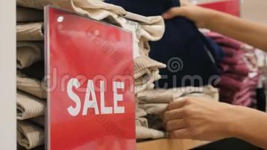 女手从服装店挑选裤子。 购物中心的大红色标志。 4K.