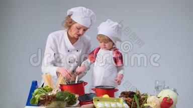 可爱的小男孩和他美丽的母亲在厨房做饭时微笑。 年轻的家庭在厨房做饭。 青年