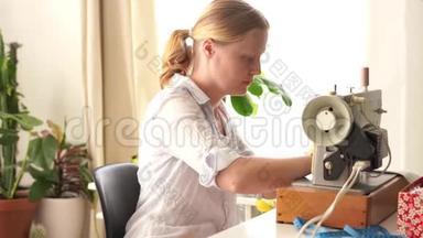 在家工作。 年轻的金发女人在明亮的房间里用打字机<strong>缝衣服</strong>