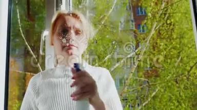 一个年轻女人打扫房子的肖像。 洗窗户，窗外是春天-绿色的树枝。