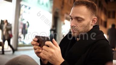 年轻的帅哥晚上在咖啡馆里度过闲暇时光，使用带有触摸屏的智能手机。
