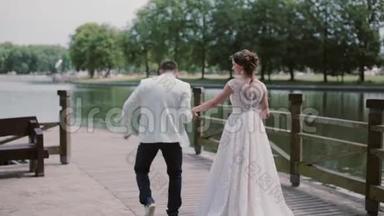 很棒的一对夫妇穿着结<strong>婚礼服</strong>走在码头上。 他们牵手，聊天，玩得开心。 美丽的大自然。 背面