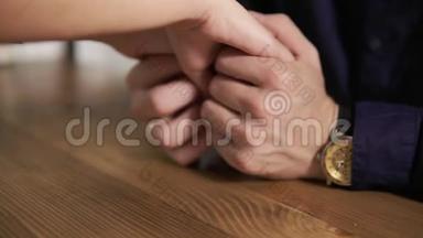 一对年轻夫妇手牵手坐在木桌旁的特写镜头。 相亲相爱的情侣