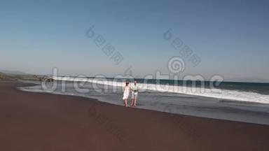 4K航天飞行视频的年轻夫妇在海滩与黑色火山沙在日落时间。 巴厘岛。