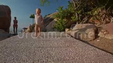 小女孩从母亲那里沿着海滩上的落基小径奔跑