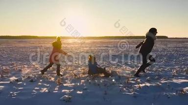 十几岁的女儿和母亲拉着小儿子在雪橇上跑。 剪影一家人在冬天玩。 积极健康