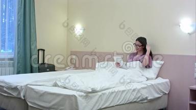 一个年轻漂亮的女孩子躺在一个旅馆房间里，躺在床上，用平板电脑聊天，视频聊天会议