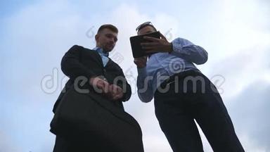 两位年轻商人在户外聊天和使用平板电脑。 商人们在外面的天空中<strong>工作</strong>