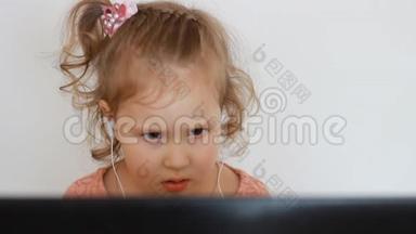 一个戴着耳机的小可爱女孩看着屏幕监视器电脑.. 看电视、录像、卡通或玩游戏的滑稽儿童