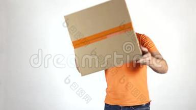 送货员穿着橙色制服，朝镜头扔了一个大包裹。 浅灰色背景，慢镜头拍摄