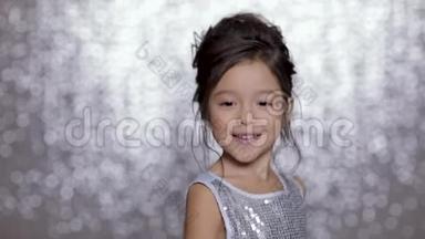 美丽的微笑的小女孩，穿着银色的裙子，在银色的背景下跳舞。