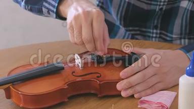 穿格子衬衫的年轻人的特写双手正在修理坐在桌子旁的小提琴。