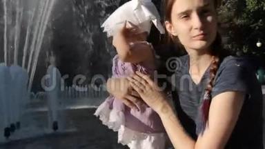 一个年轻的保姆在喷泉旁抱着孩子