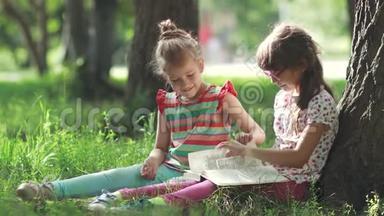 两个小女孩在<strong>树下</strong>享受晴天和<strong>看书</strong>。 姐姐给妹妹读一本书